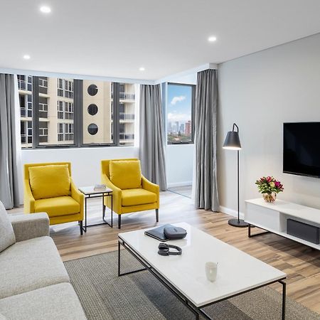 Meriton Suites Bondi Junction Sidney Dış mekan fotoğraf The photo shows a modern, well-lit living room. It features a light gray sofa with a textured fabric. There are two bright yellow armchairs positioned near a window, which allows natural light to enter the space. The room has light gray curtains and 