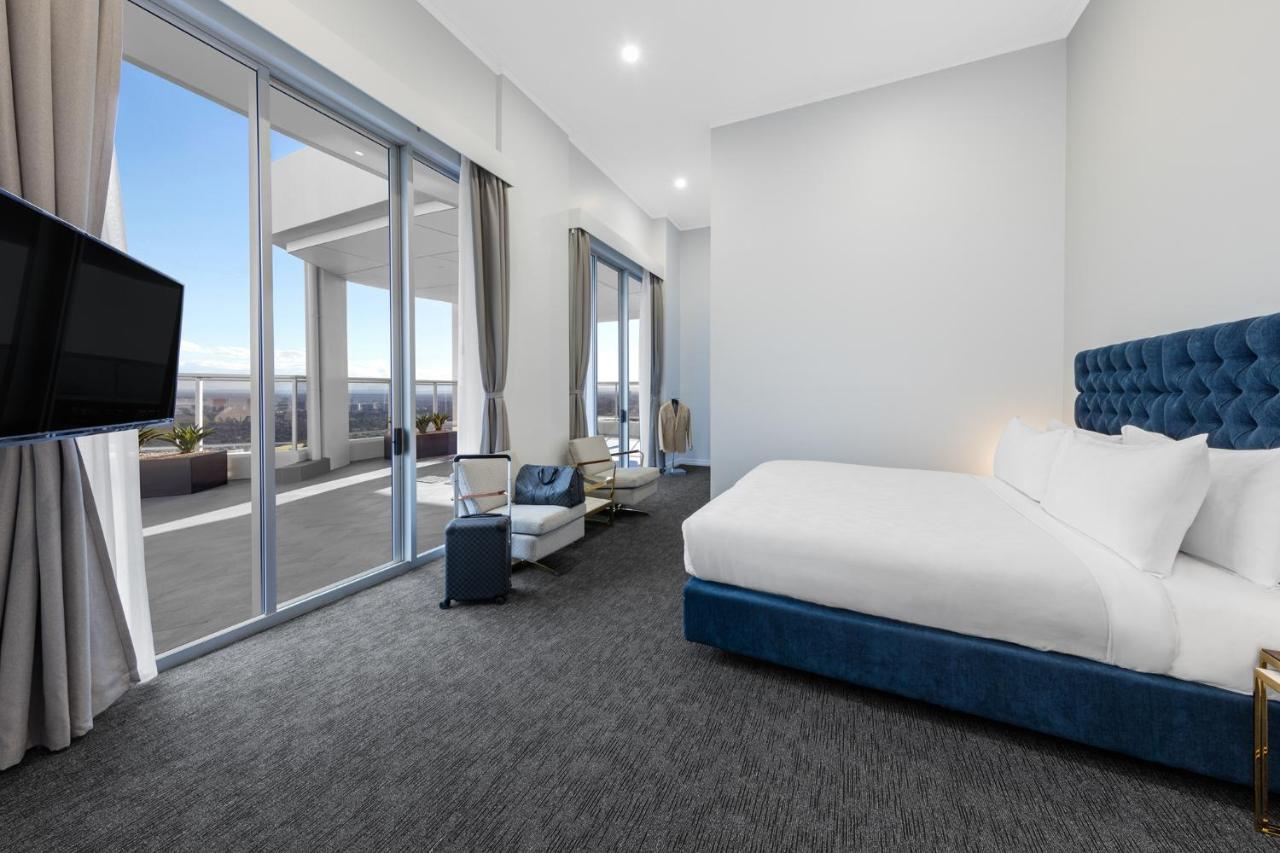 Meriton Suites Bondi Junction Sidney Dış mekan fotoğraf The photo shows a modern and spacious hotel room. It features a large bed with a blue headboard, a flat-screen TV mounted on the wall, and a cozy seating area with a chair and small table. The room has large windows that offer natural light and a vie