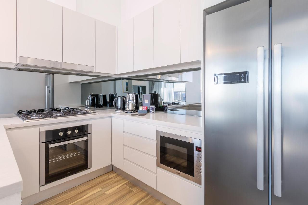 Meriton Suites Bondi Junction Sidney Dış mekan fotoğraf The photo shows a modern kitchen with a clean and minimalist design. It features white cabinetry and a stainless steel refrigerator. The kitchen includes a gas stove with an oven below it, as well as a microwave. There are several kitchen appliances,
