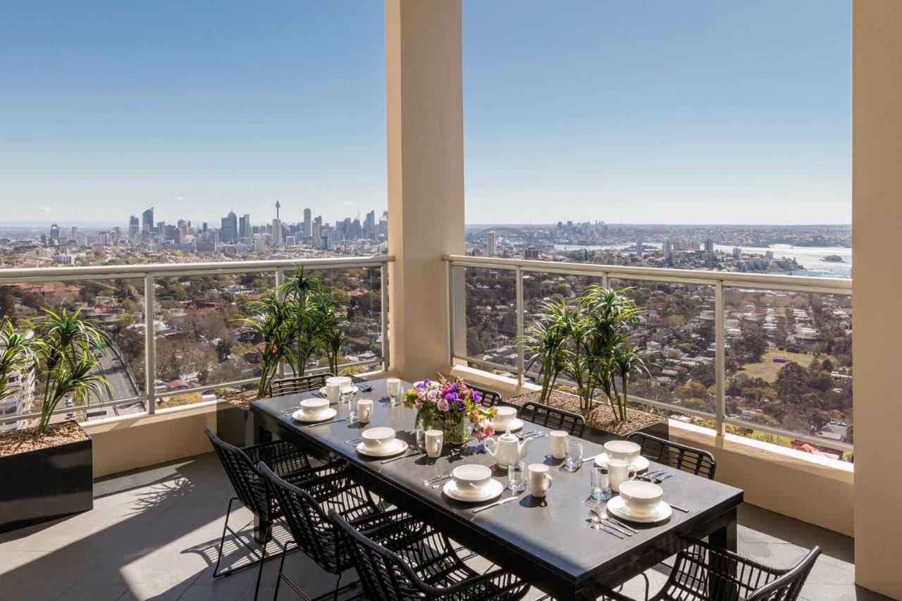 Meriton Suites Bondi Junction Sidney Dış mekan fotoğraf The photo shows a beautifully arranged outdoor dining area on a balcony. There is a long black dining table set for a meal, with plates, glasses, and decorative items like a vase of flowers. Surrounding the table are stylish black chairs. In the back