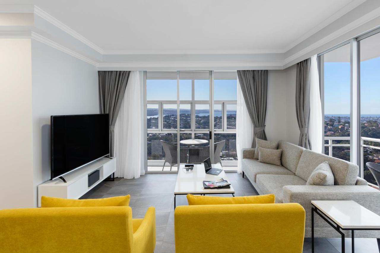 Meriton Suites Bondi Junction Sidney Dış mekan fotoğraf The photo depicts a modern living room space with large windows that offer a view of the outside. The decor is minimalist and stylish, featuring a light color palette. 

In the center, there are two bright yellow chairs facing each other. A sleek, re