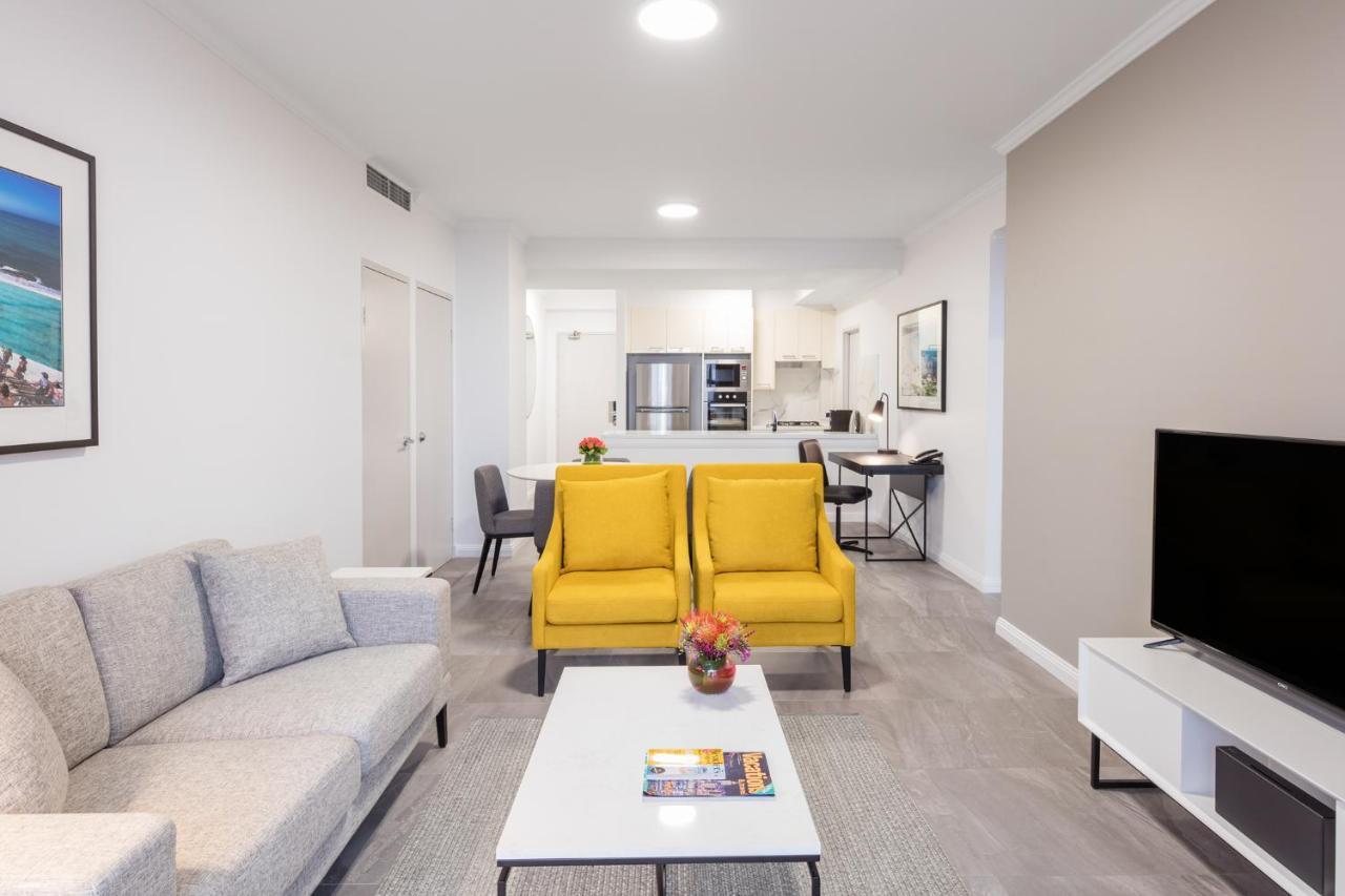 Meriton Suites Bondi Junction Sidney Dış mekan fotoğraf The photo shows a modern living space with a light and airy design. In the foreground, there are two bright yellow armchairs flanking a white coffee table, which has a small vase of flowers and a magazine on it. To the left, there is a light gray sof