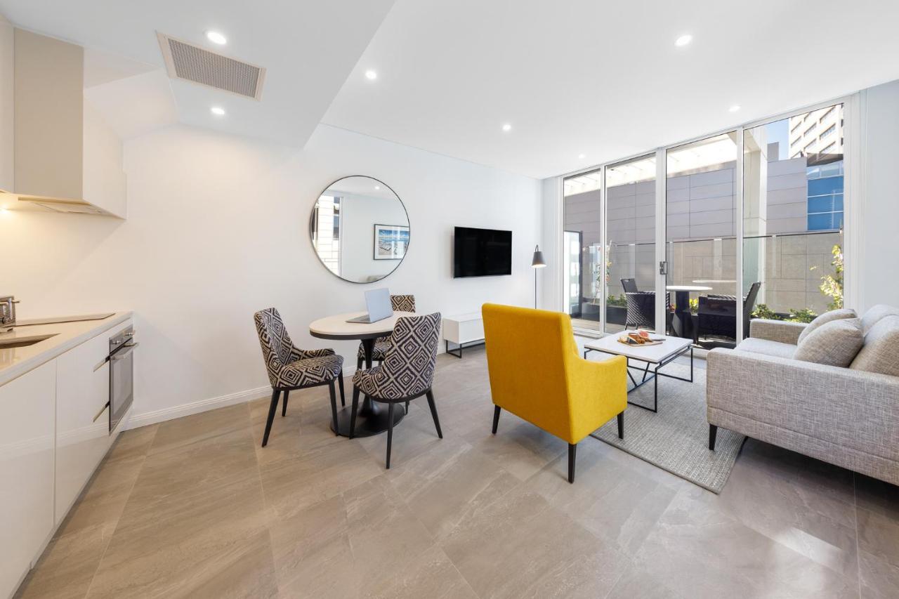 Meriton Suites Bondi Junction Sidney Dış mekan fotoğraf The photo shows a modern and stylish living space. On one side, there is a kitchen area with sleek cabinetry, and next to it, a round dining table surrounded by three patterned chairs. In the center of the room, there is a gray sofa accompanied by a 