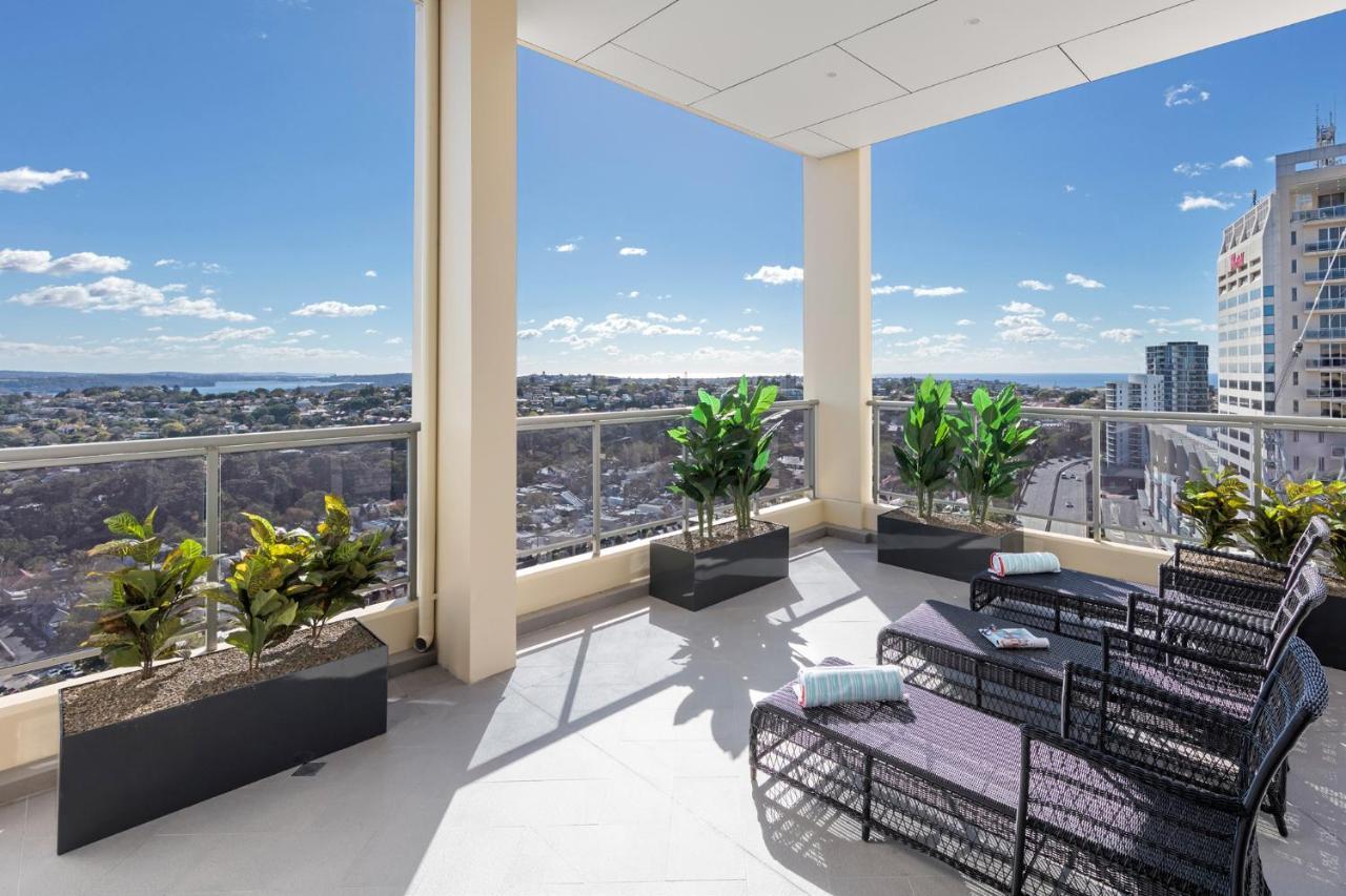 Meriton Suites Bondi Junction Sidney Dış mekan fotoğraf The photo shows a modern balcony or terrace area with a stunning view. There are several planters with green plants placed along the edge. The seating area features lounge chairs in a contemporary design, likely made of woven materials. The space app