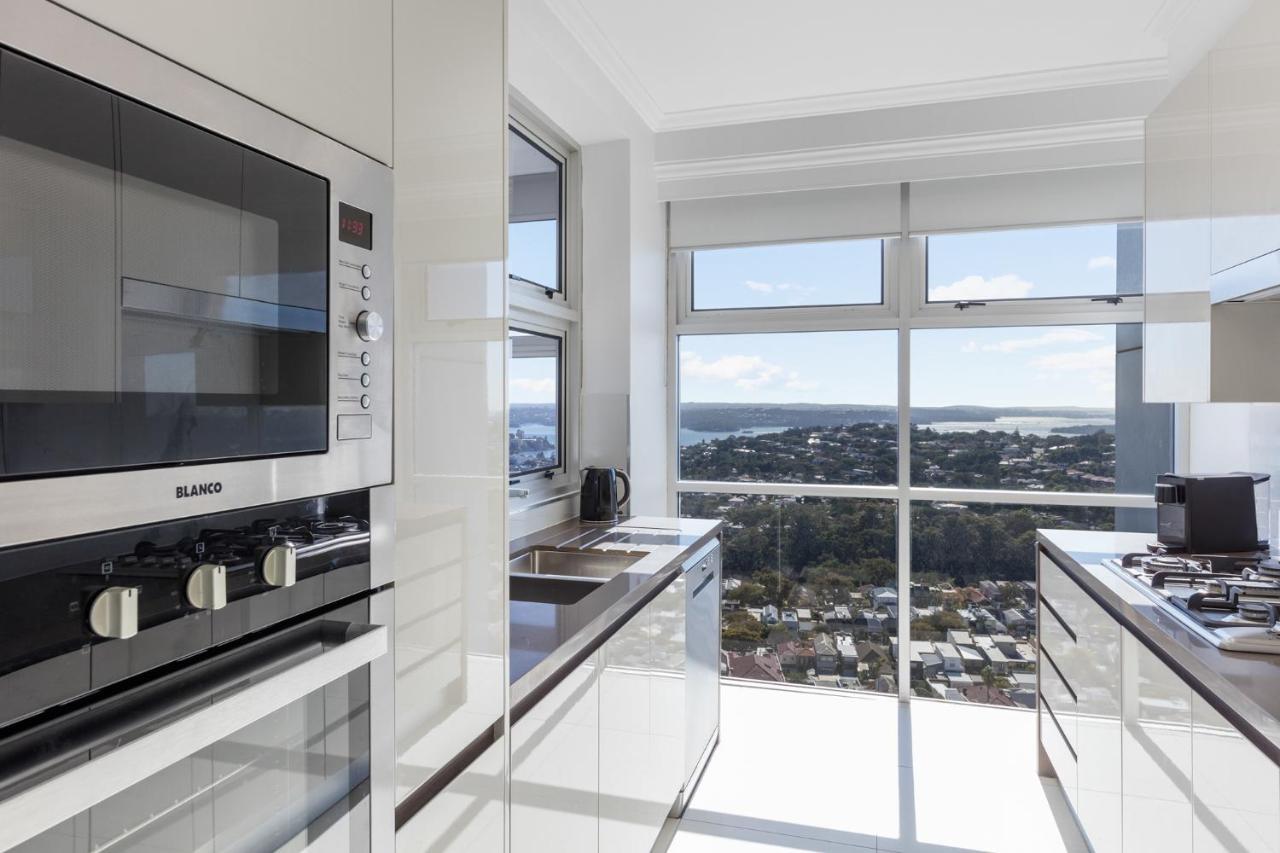 Meriton Suites Bondi Junction Sidney Dış mekan fotoğraf The photo shows a modern kitchen with sleek, shiny white cabinets and a large window that offers a panoramic view of the outside landscape. The kitchen features built-in appliances, including an oven and a stove, with a stylish countertop. The spacio