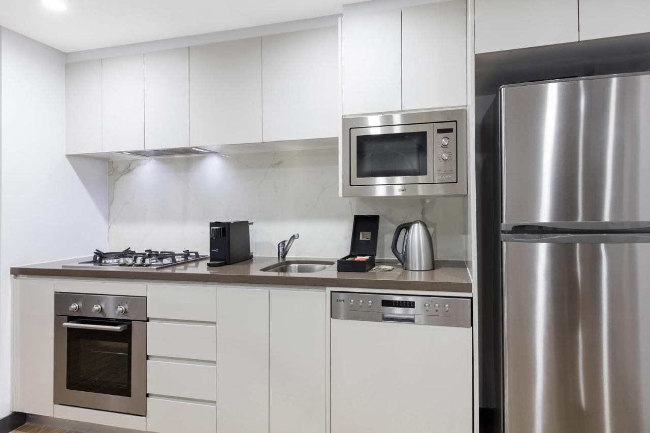 Meriton Suites Bondi Junction Sidney Dış mekan fotoğraf The photo shows a modern kitchen with a sleek, minimalist design. It features white cabinetry and a countertop that blends with the overall aesthetic. 

Key elements include:

- A stainless steel refrigerator on the right.
- An oven with a gas cookto