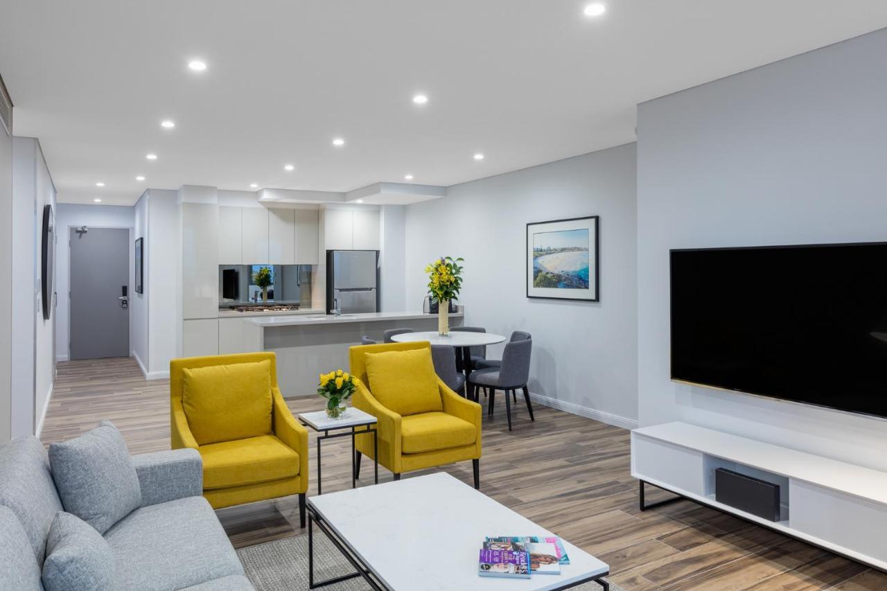 Meriton Suites Bondi Junction Sidney Dış mekan fotoğraf The photo shows a modern living space that includes a cozy sitting area and a dining area. The sitting area features two bright yellow chairs and a light gray sofa, arranged around a coffee table. There are decorative items on the table, including fl