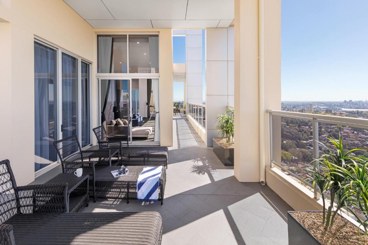 Meriton Suites Bondi Junction Sidney Dış mekan fotoğraf The photo shows a spacious balcony or terrace area of a high-rise building. It features modern outdoor furniture, including a seating arrangement with dark wicker chairs and a table. There are cushions, and a blue and white striped blanket is draped 