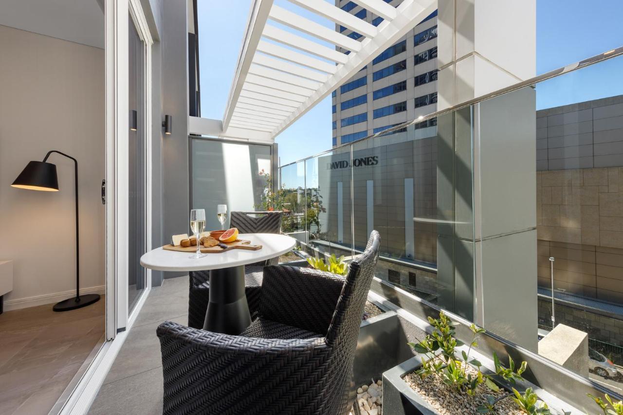 Meriton Suites Bondi Junction Sidney Dış mekan fotoğraf The photo shows a modern balcony area with glass railings. It features a small round table set for two, with a plate of food and drinks. There are two stylish wicker chairs positioned around the table. The space is bright and airy, with sunlight stre