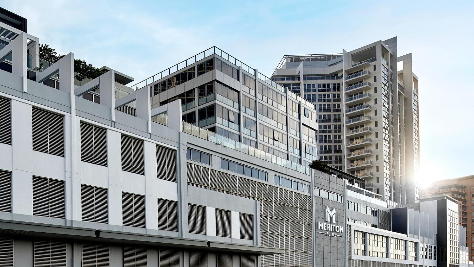 Meriton Suites Bondi Junction Sidney Dış mekan fotoğraf The image shows a modern urban building or complex. The structure features a combination of glass and concrete elements, showcasing contemporary architectural design. The foreground has a lower section that appears to be a podium or base with a textu