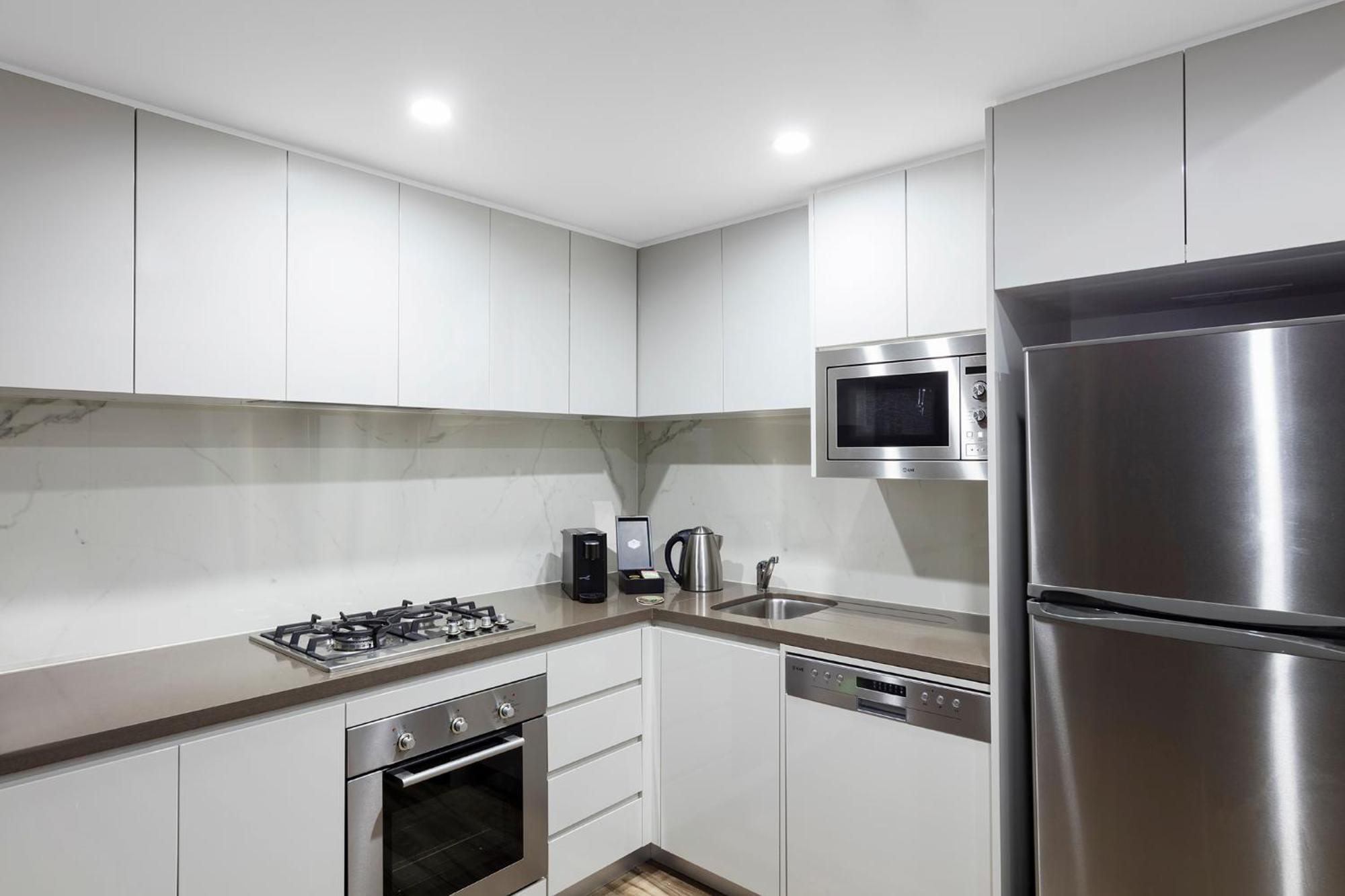 Meriton Suites Bondi Junction Sidney Dış mekan fotoğraf The photo shows a modern kitchen featuring a minimalist design. It has light-colored cabinetry, a countertop, and stainless steel appliances. The appliances include a gas stove with multiple burners, an oven, a microwave, a kettle, and a refrigerator