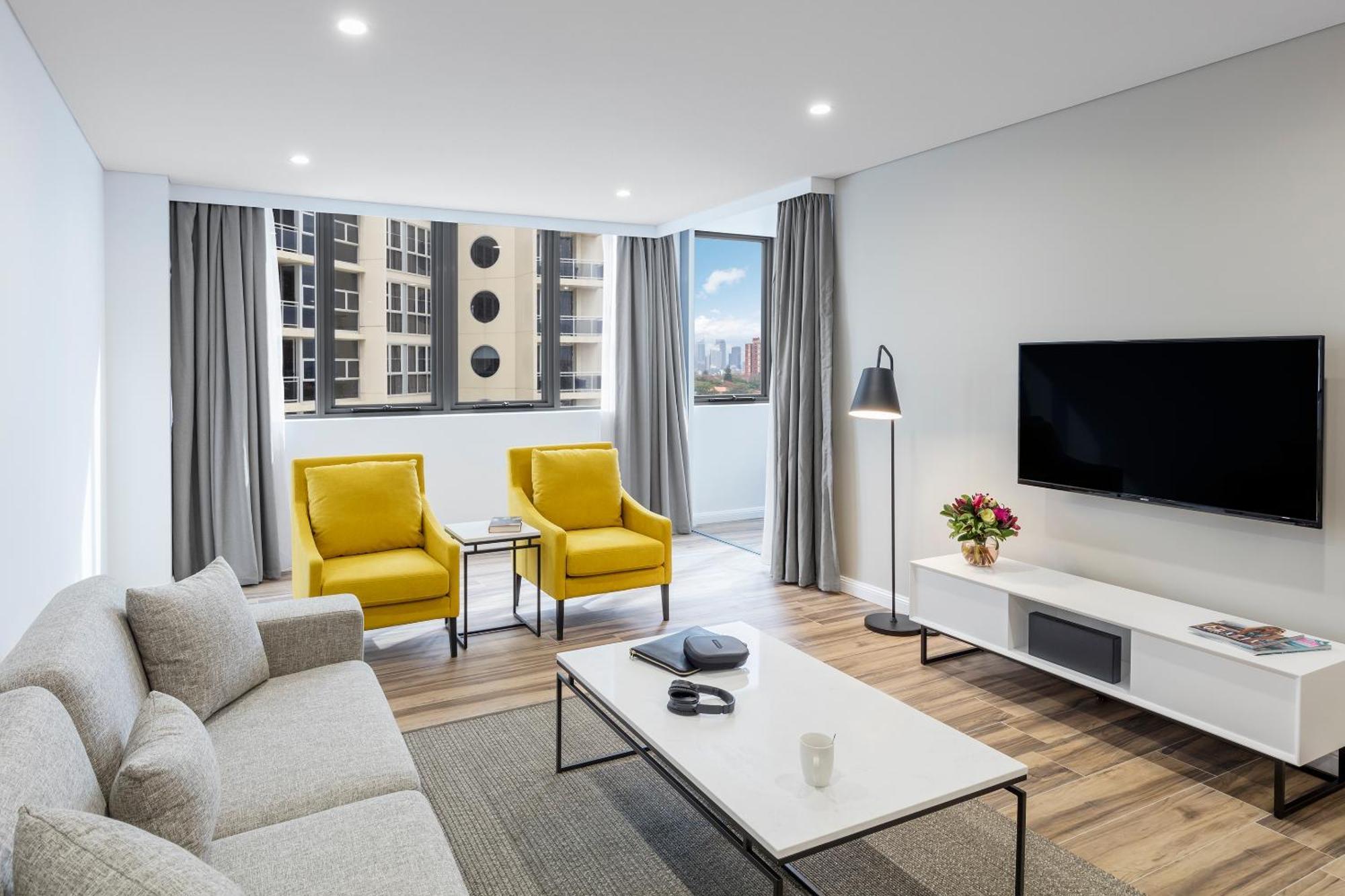 Meriton Suites Bondi Junction Sidney Dış mekan fotoğraf The photo shows a modern, well-lit living room. It features a light gray sofa with a textured fabric. There are two bright yellow armchairs positioned near a window, which allows natural light to enter the space. The room has light gray curtains and 